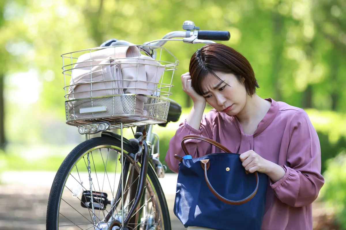 自転車の横でバッグの中を探し、鍵が見つからず困っている女性